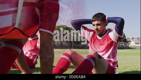 Der leistungsfähige Sit-up-Athlet trägt rot-weißes Fußballtrikot auf dem Rasenfeld, mit Lätzchen und Kopierraum Stockfoto