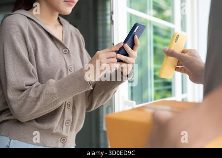 Glückliche asiatische Frau scannt QR-Code für Warenlieferung. Liefermann schickt Lieferexpress. Online-Shop, Papierbehälter, zum Mitnehmen, Postbote, Lieferservice Stockfoto