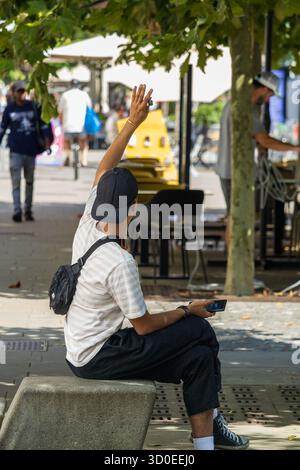 Ljubljana, Slowenien August 10-2025 Ein Mann sitzt auf einer Bank, der eine Hand hebt, um einen Freund zu begrüßen Stockfoto