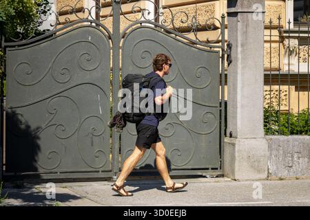 Ljubljana, Slowenien August 10-2025 Person mit Rucksack, die am kunstvollen Metalltor vorbeigeht Stockfoto