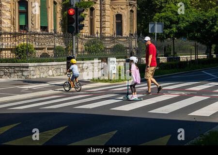 Ljubljana, Slowenien 10. August 2025 – Familie überquert die Straße mit Helmen und Grün im Hintergrund mit Erwachsenen und Kindern auf dem Fahrrad Stockfoto