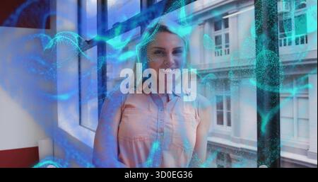 Lächelnde Frau mit pfirsichfarbenem Oberteil am Bürofenster in der Nähe der roten Fensterbank als blau-grüner Überzug, der wirbelt Stockfoto