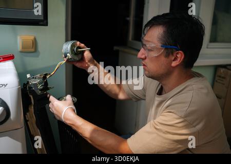 Ein spezialisierter Techniker mit Schutzbrille und Handschuhen untersucht die Komponenten der zerlegten Waschmaschine und konzentriert sich dabei auf den abgetrennten Motor Stockfoto