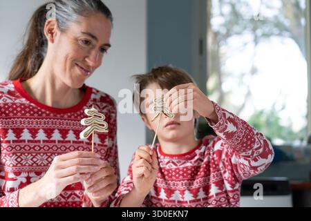 Mutter und Sohn tragen festliche Pyjamas und halten Desserts in Form eines weihnachtsbaums auf Spießen Stockfoto