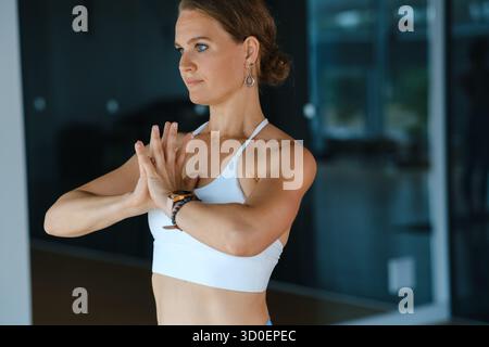 Eine fitte Frau spielt eine Yoga-Pose in einem gut beleuchteten Studio und zeigt ihre Konzentration und Balance. Sie trägt bequeme Kleidung und verkörpert Ruhe Stockfoto