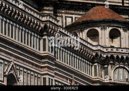Komplexe Mischung aus weißem, grünem und rosa-rotem toskanischem Marmor, eingelegt in Streifen, Bändern und Tafeln auf der Südseite der Renaissance-Kathedrale oder des Duomo di Firenze in Florenz, Toskana, Italien. Das komplizierte Design umfasst spitze gotische Bögen, geformte Konsolen, abgerundete Nischen mit Muschelkopf und eine kleine Kuppel mit roten Terrakottafliesen. Stockfoto
