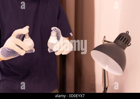 Zwei Glühlampen mit unterschiedlichen Sockel: E14 und E27. Konzept der Wahl der richtigen Glühlampengröße. Nahaufnahme der Hände im Schutzhandschuh bei der Wartung Stockfoto