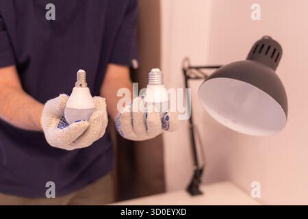 Zwei Glühlampen mit unterschiedlichen Sockel: E14 und E27. Konzept der Wahl der richtigen Glühlampengröße. Nahaufnahme der Hände im Schutzhandschuh bei der Wartung Stockfoto