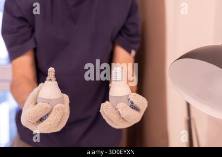 Zwei Glühlampen mit unterschiedlichen Sockel: E14 und E27. Konzept der Wahl der richtigen Glühlampengröße. Nahaufnahme der Hände im Schutzhandschuh bei der Wartung Stockfoto