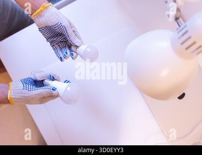 Zwei Glühlampen mit unterschiedlichen Sockel: E14 und E27. Konzept der Wahl der richtigen Glühlampengröße. Nahaufnahme der Hände im Schutzhandschuh bei der Wartung Stockfoto