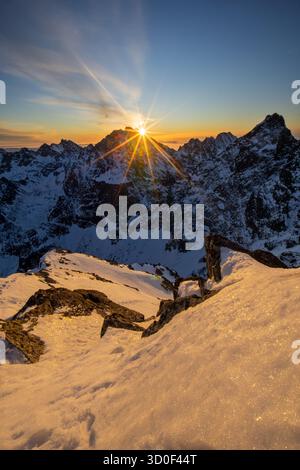 Aus der Vogelperspektive des Sonnenstrahls über den schneebedeckten Gipfeln, der einen goldenen Glanz über die zerklüftete Landschaft des Rysy-Gipfels in der Hohen Tatra in der Slowakei wirft. Stockfoto