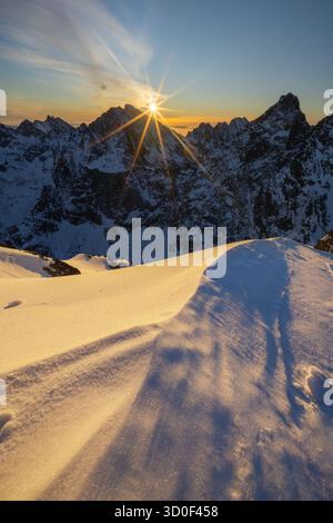 Aus der Vogelperspektive blickt die Sonne über den schneebedeckten Rysy-Gipfel und wirft lange Schatten über die unberührte, hügelige Schneelage in der Hohen Tatra, Slowakei. Stockfoto