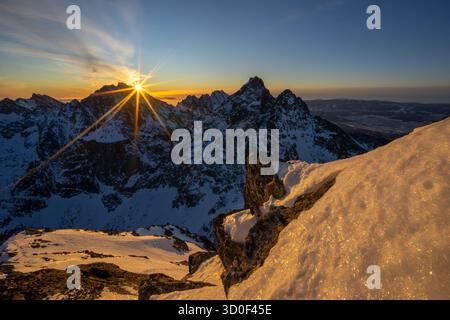 Aus der Vogelperspektive auf den schneebedeckten Rysy-Gipfel, der die klare, zerklüftete Landschaft mit einem warmen, goldenen Leuchten beleuchtet, hohe Tatra, Slowakei. Stockfoto
