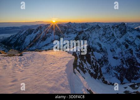 Aus der Vogelperspektive des Sonnenstrahls über den schneebedeckten Gipfeln von Rysy, der einen goldenen Glanz über die schroffe weiße Landschaft, Tatranska Javorina, hohe Tatra, Slowakei, ausstrahlt. Stockfoto