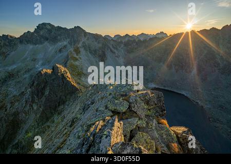Die strahlenden Finger der Sonne erstrecken sich aus der Vogelperspektive über die zerklüfteten Gipfel und den ruhigen See und malen die Landschaft in Gold- und Schattentönen, Vysoke Tatry, Presovsky kraj, Slowakei. Stockfoto