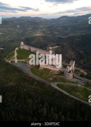Aus der Vogelperspektive auf Rocca Maggiore's beeindruckende Steinmauern umschließen den Hügel unter dem Himmel der Dämmerung und zeigen die mittelalterliche Festung Assisi, Umbrien, Italien. Stockfoto