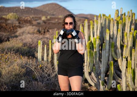 Junge Frau mit schwarzem ärmellosem Sporttop, schwarzen Shorts und Boxhandschuhen in schwarz-weiß, die ihre Fäuste in einer defensiven Haltung hochhalten Stockfoto