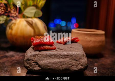 Kunstvoll angeordnete rote Känguruscheiben, garniert mit essbaren Ameisen, präsentiert auf einem dunklen Stein, in einer eleganten Nachtkulisse. Stockfoto