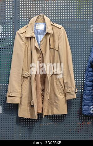 Beigefarbener Regenmantel, der bei Fence Classic Herrenmode hängt Stockfoto