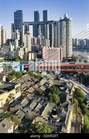 Blick aus der Vogelperspektive auf die traditionellen Dächer der Gildenhalle Huguang, eingebettet vor der modernen Skyline und den Raffles City-Wolkenkratzern, Chongqing, China. Stockfoto