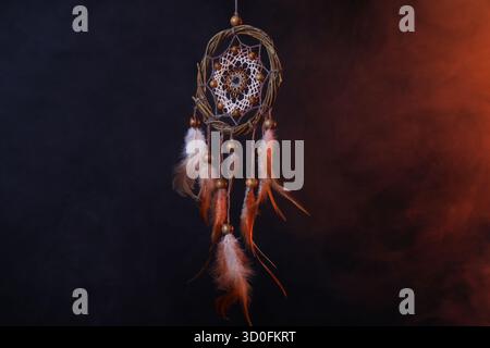 Wunderschöner Traumfänger, der in farbigen Lichtern auf dunklem Hintergrund mit Rauch hängt Stockfoto