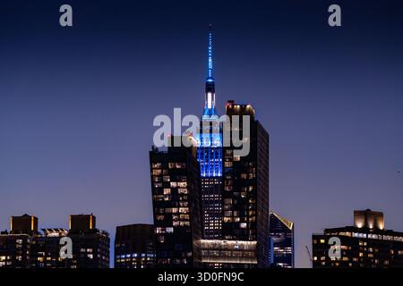 Blick auf das majestätische Empire State Building, das in leuchtendem Blau vor dem dunklen Dämmerhimmel beleuchtet ist, dessen majestätische Präsenz die Stadt dominiert Stockfoto