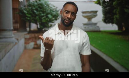 Der Mann zeigt den Daumen zur Seite und zeigt den Unterarm vor dem Gebäude und dem Steinpflanzengang; stiller Zweifel. Stockfoto