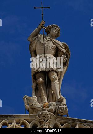 Der gepanzerte Heilige Michael der Erzengel besiegt das Böse, indem er den gehörnten und mit Klauen besetzten Satan tötet, ihn mit einem christlichen Kreuz aus Metall aufspießt und gleichzeitig den gefallenen Engel mit Füßen trampelt. Herrliche Steinstatue aus dem Jahr 1507 n. Chr., von dem burgundischen Bildhauer Jean Paumier, auf der Spitze des extravaganten gotischen Westgiebels der mittelalterlichen Cathédrale de St.-Sauveur in Aix-en-Provence, Provence-Alpes-Côte d’Azur, Südfrankreich. Stockfoto