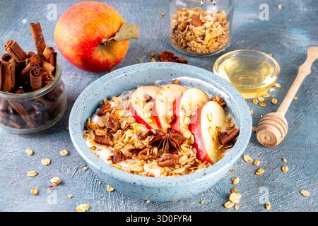 Gesundes Herbstfrühstück oder Snack, Schüssel mit griechischem Joghurt, Müsli, Äpfeln, Honig und Pekannüsse, auf blauem Betonhintergrund mit Zutat, Kopierraum Stockfoto