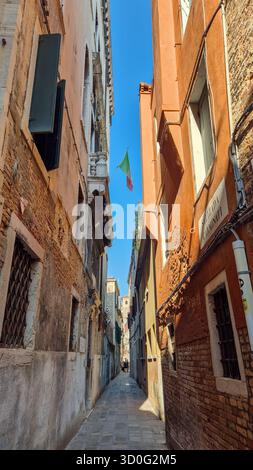 Enge Gasse in Venedig, Italien mit hängender italienischer Flagge, historischer Straße und traditioneller Architektur. Stockfoto
