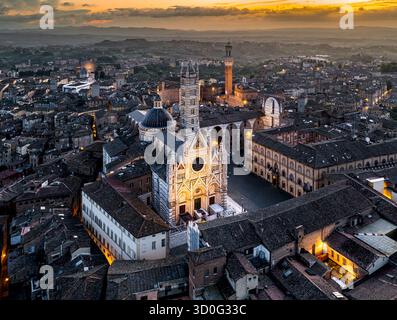 Aus der Vogelperspektive erhebt sich der beleuchtete Duomo di Siena und der Torre del Mangia majestätisch inmitten der alten Dächer, die mit warmen Dämmertönen bemalt sind, Siena, Toskana, Italien. Stockfoto