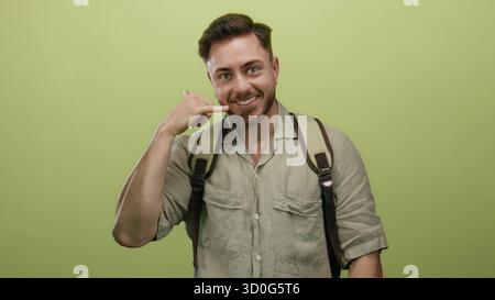 Ein junger Mann mit Bart und Rucksack-Gesten ruft mich an, vor einem isolierten gelben Hintergrund, der zuversichtlich auf die Kamera zeigt und auf den spiri eines Reisenden Stockfoto