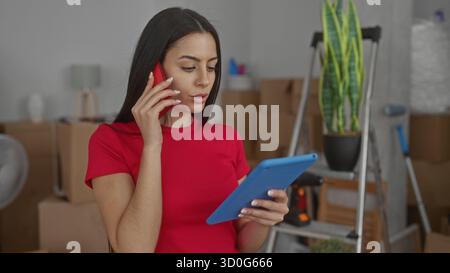Multitasking von Frauen in einem neuen Zuhause mit Telefon und Tablet, umgeben von Umzugskästen und Pflanzen im Wohnzimmer. Stockfoto