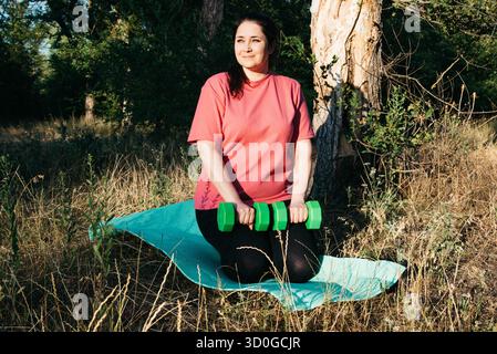 Eine große Frau, die im Freien Hantelübungen macht. Outdoor-Sport. Grüne Kurzhanteln in den Händen des Athleten. Hochwertige Fotos Stockfoto