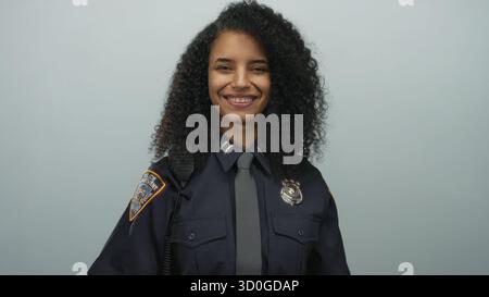 Hispanische Polizistin in Uniform streckt einen Handschlag und lächelt selbstbewusst vor weißem Hintergrund. Stockfoto
