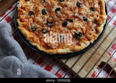 Frisch gebackene hausgemachte Pizza mit schwarzen Oliven und geschmolzenem Käse auf einem Kühlregal Stockfoto