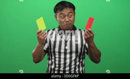 Der Schiedsrichter hält die rote und gelbe Karte und pfiff auf dem Schlüsselband in grünem Studio; Fairness. Stockfoto