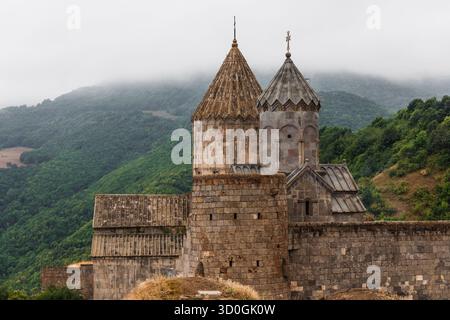 Der Blick auf die antiken Steine des Klosters Tatev erhebt sich vor dem Hintergrund grüner Berge, die in Nebel gehüllt sind, und schafft eine zeitlose Szene, Tatew, Provinz Syunik, Armenien. Stockfoto