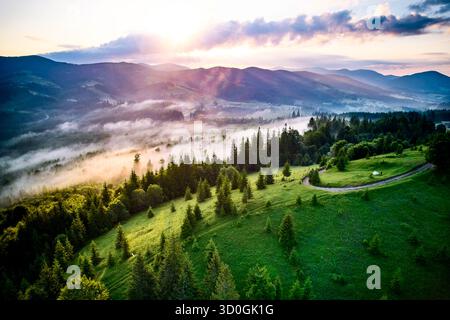 Atemberaubender Blick aus der Luft auf das üppige grüne Tal bei Sonnenaufgang, wo Morgennebel anmutig über die Landschaft schwingt. Sonnenstrahlen strahlen strahlen goldenes Leuchten und schaffen eine ruhige und malerische Szene. Stockfoto