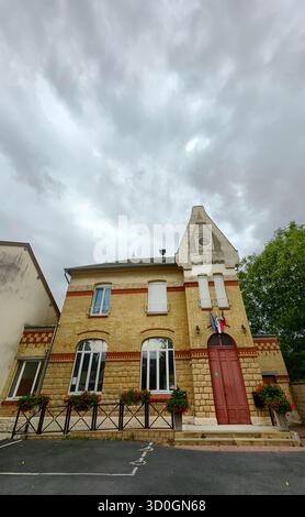 Bergnicourt, Rethel, Ardennes, Grand-Est, Frankreich, August, 28. August 2025, Ein charmantes zweistöckiges Gebäude mit leuchtenden Blumen zeigt stolz eine französische Flagge unter einem bewölkten Himmel Stockfoto