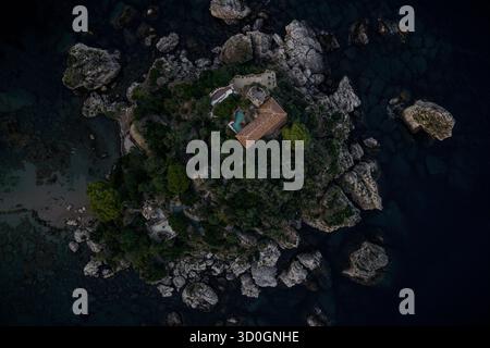 Blick aus der Vogelperspektive auf eine einsame Villa, eingebettet in die zerklüftete, felsige Küste, umgeben vom tiefblauen Meer, Isola Bella, Taormina, Sizilien, Italien. Stockfoto