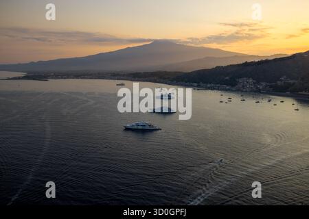 Aus der Vogelperspektive von Yachten, die auf dunklem Wasser schwimmen, mit dem Ätna, der in den sanften Tönen der untergehenden Sonne gemalt ist, Sizilien, Italien. Stockfoto