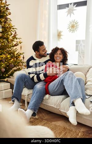 Ein glückliches Paar teilt Liebe und Lachen, während es Weihnachten an einem geschmückten Baum feiert. Stockfoto