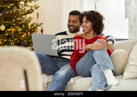 Ein fröhliches afroamerikanisches Paar genießt die Gesellschaft des anderen, während es zu Hause Weihnachten feiert. Stockfoto