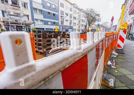 Eine Baustelle in einer Stadtstraße, umgeben von orangen Barrieren mit Warnschildern und verstreuten Materialien Stockfoto