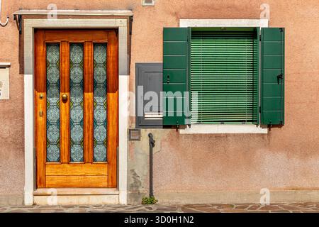 Eine Holztür und ein Fenster mit grünen Holzläden und grünen Jalousien in einer Straße im Santa Croce Sestiere von Venedig, Italien Stockfoto