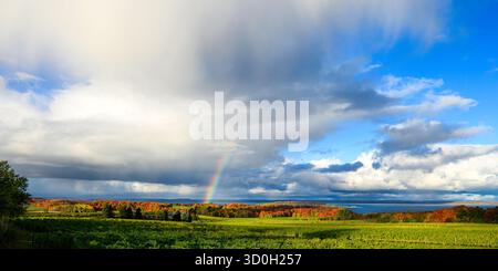 Ein Regenbogen über der West Grand Traverse Bay im Herbst mit bunten Blättern auf den Bäumen auf der Old Mission Peninsula und Power Island, Michigan, USA. Stockfoto
