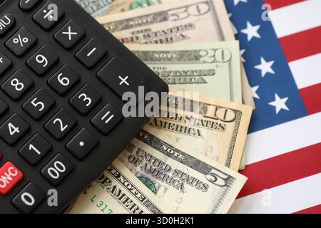 US-Dollar-Geldscheine und Taschenrechner auf amerikanischer Flagge Nahaufnahme. Geldinvestitionskonzept und Steuerzahlung Stockfoto