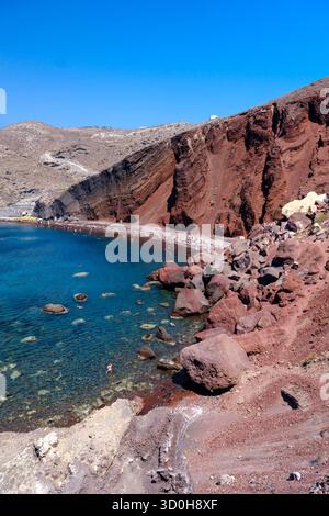 Santorini, GR - 4. September 2025: Der berühmte Rote Strand in Santorin, mit hellrotem vulkanischem Felsen und Sand neben der klaren blauen Ägäis Stockfoto