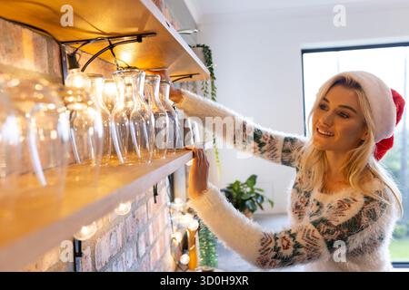 Frau mit Urlaubspullover, Weihnachtsmann-Hut, der den Glaskrug in der Küche ausrichtet, Kopierraum Stockfoto